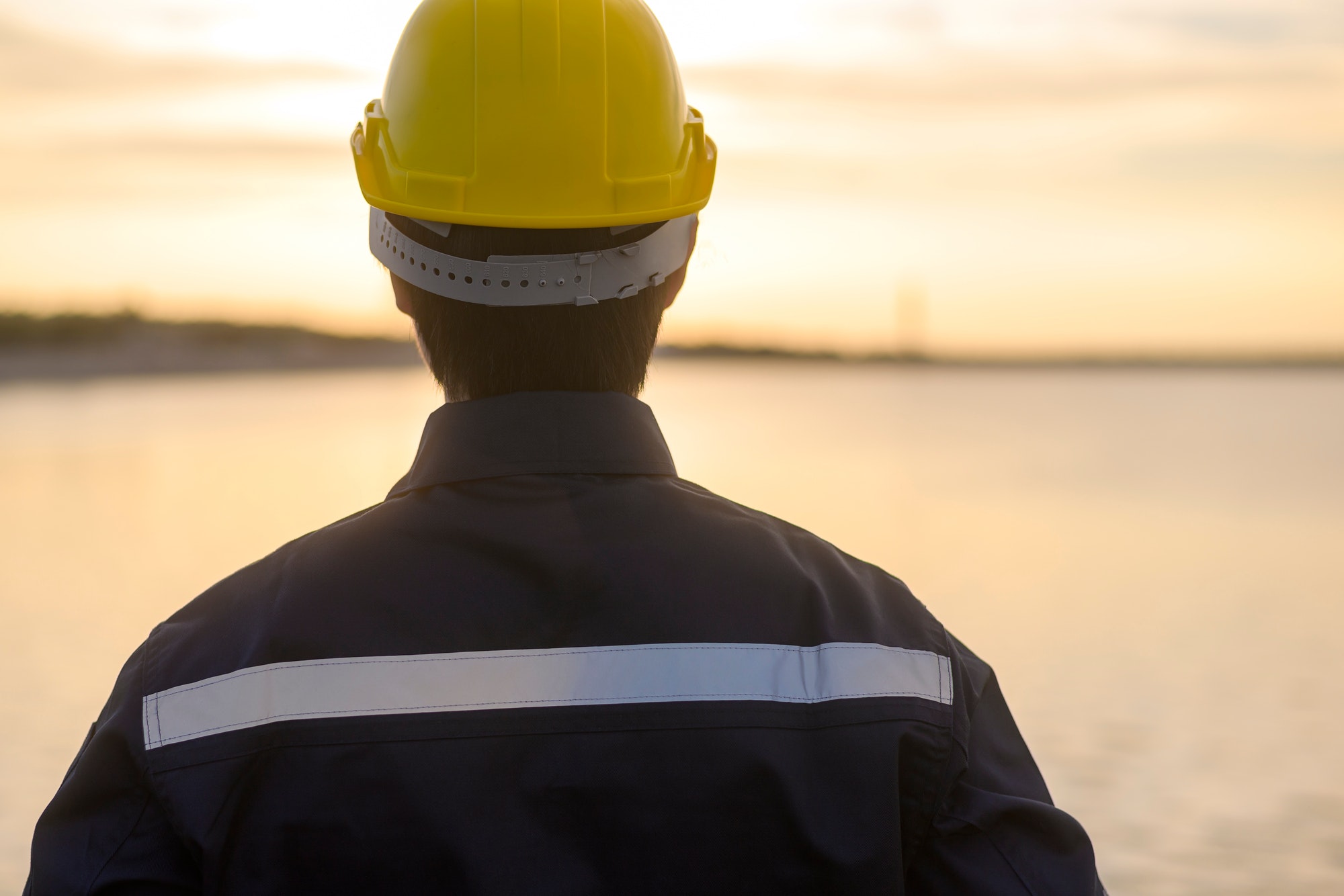 A male engineer wearing a protective helmet at sunset.